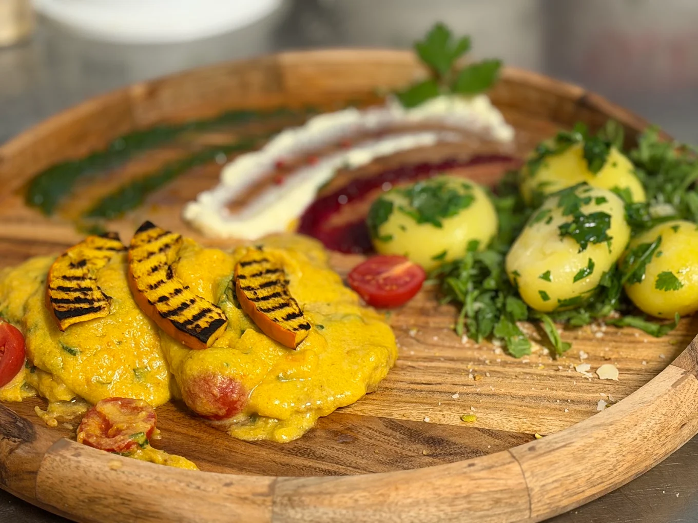 Liebevoll angerichtetes Gericht mit gegrilltem Gemüse und Kartoffeln auf einer rustikalen Holzplatte